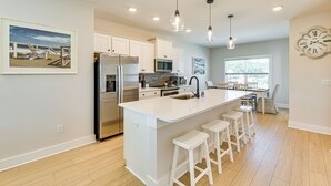 Une cuisine moderne avec des meubles blancs, des appareils en acier inoxydable et des luminaires suspendus.