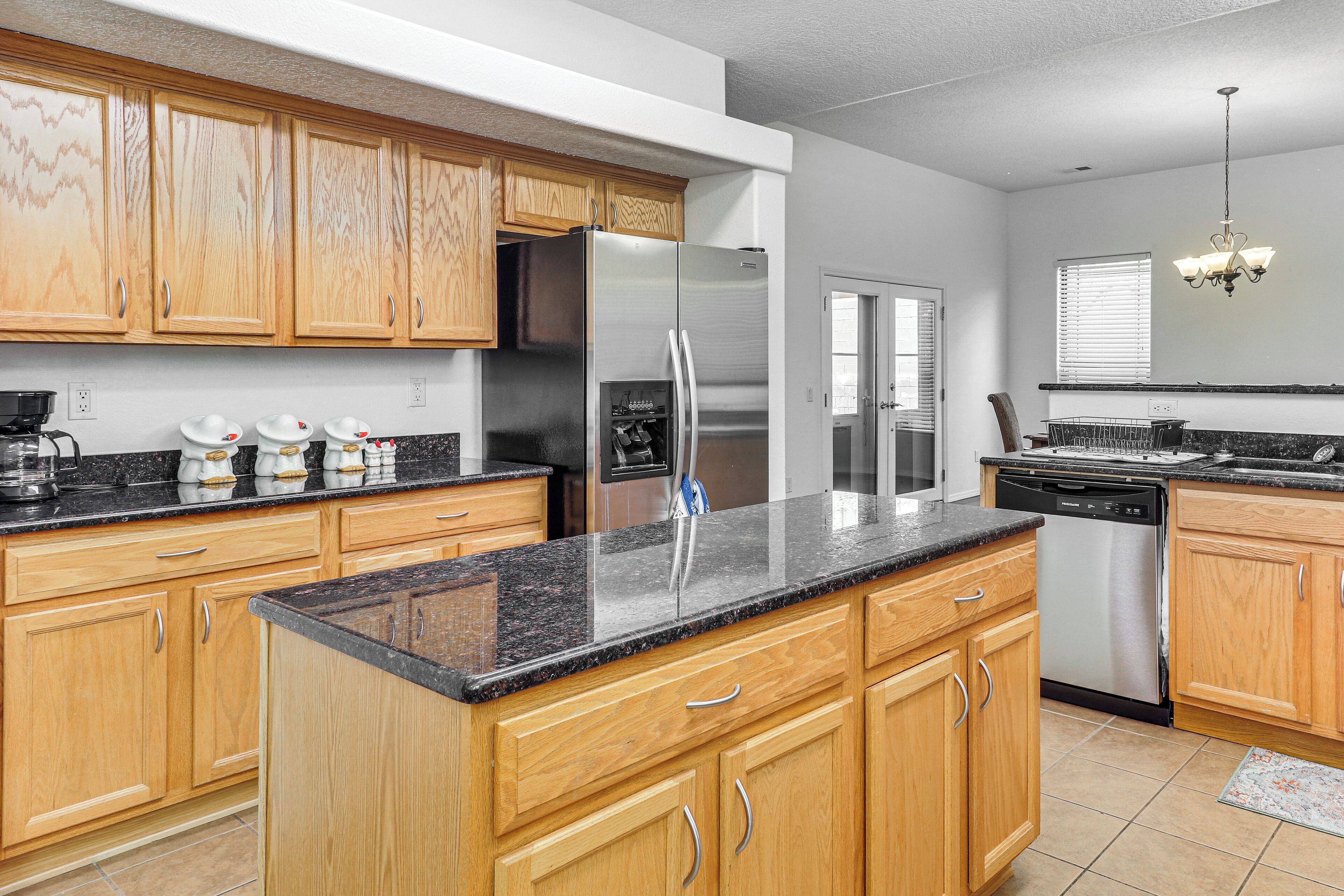 A kitchen with wooden cabinets, a stainless steel refrigerator, a dishwasher, and a granite countertop.