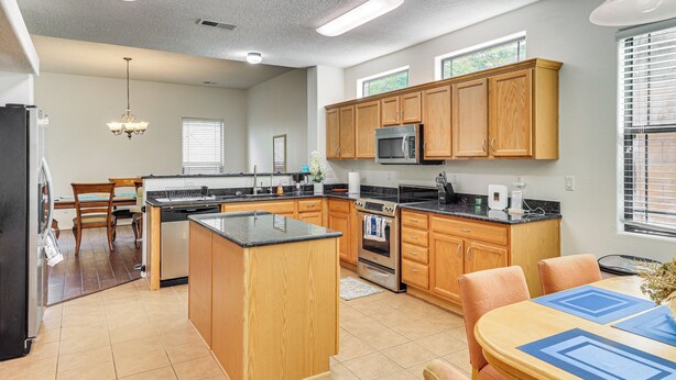 A spacious kitchen with wooden cabinets, a central island, and a dining area with a table and chairs. - Furnished Rio Rancho Rental w/ Patio & Yard (Rio Rancho)