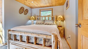 Una cama de madera con cabecera, dos lámparas de noche y una ventana con vistas a árboles.