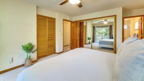 Een slaapkamer met een groot bed, een plafondventilator, houten kasten en uitzicht op een balkon.