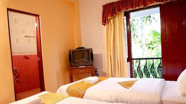 A hotel room with two beds, a television on a small table, and a balcony with a view of greenery. - Fort beach Residency (Kochi)