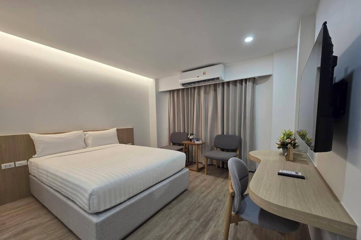 A modern hotel room with a large bed, a desk with a chair, a TV, and an air conditioning unit.