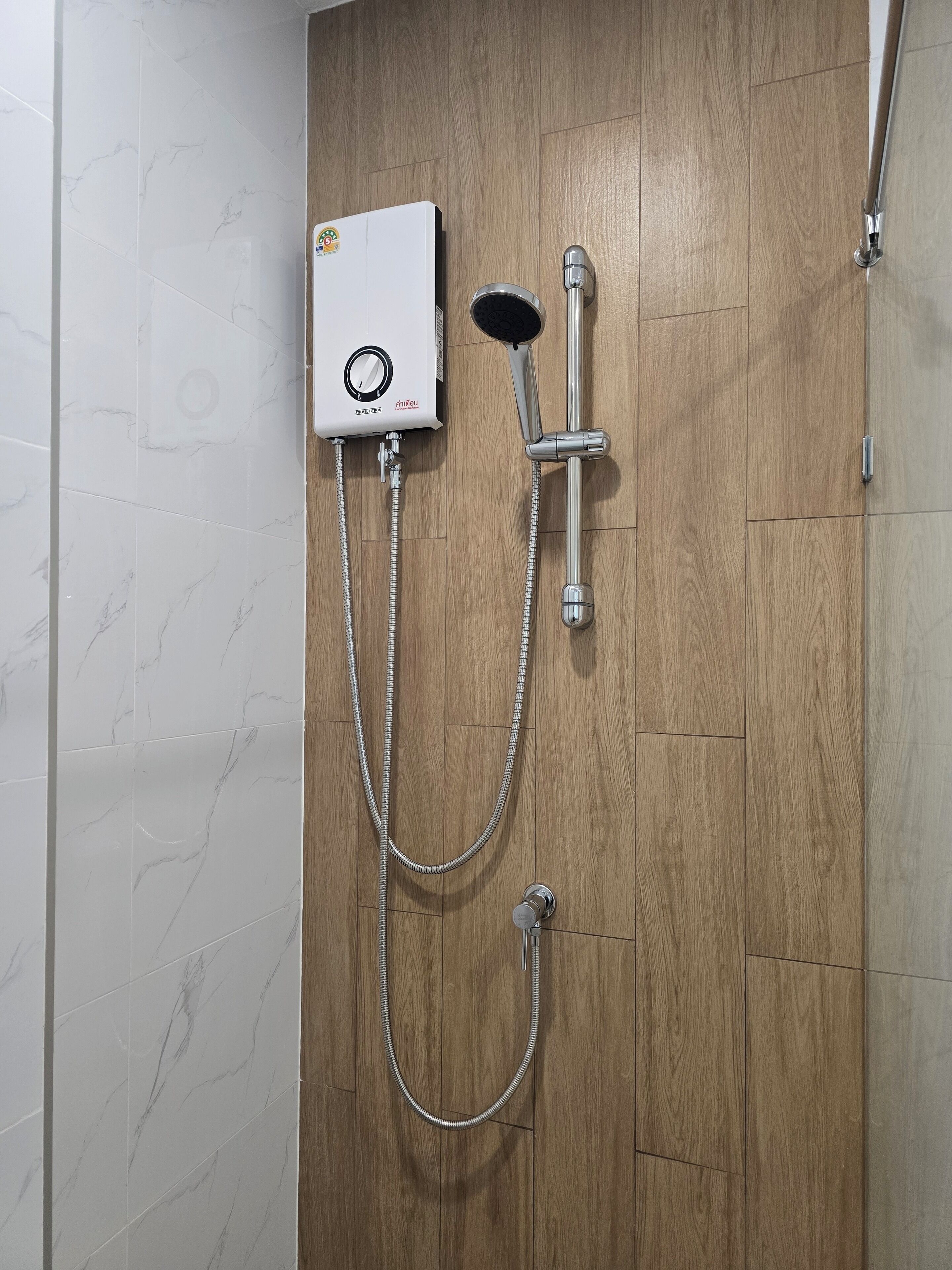 A bathroom with a shower unit mounted on a wooden wall, a handheld showerhead, and a flexible hose.