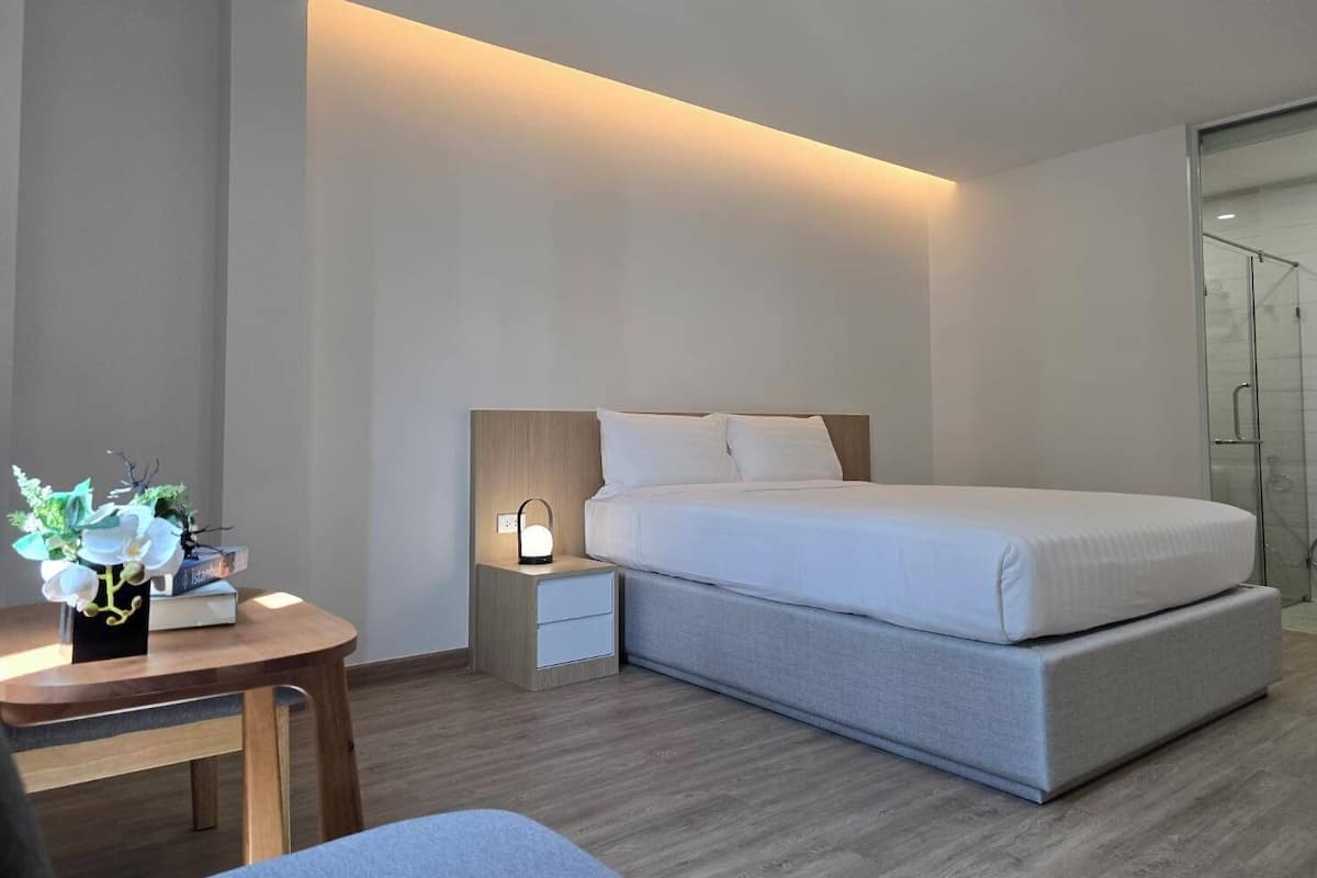A modern hotel room with a bed, bedside table, and a small desk with a lamp.