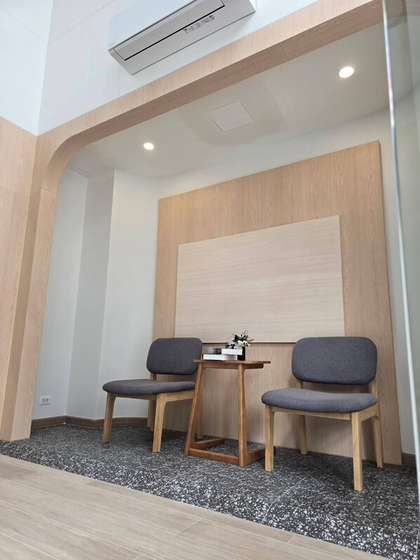 Un espace d’attente moderne avec deux fauteuils gris à revêtement en tissu, une petite table en bois ornée d’un vase et un grand mur revêtu de panneaux en bois.