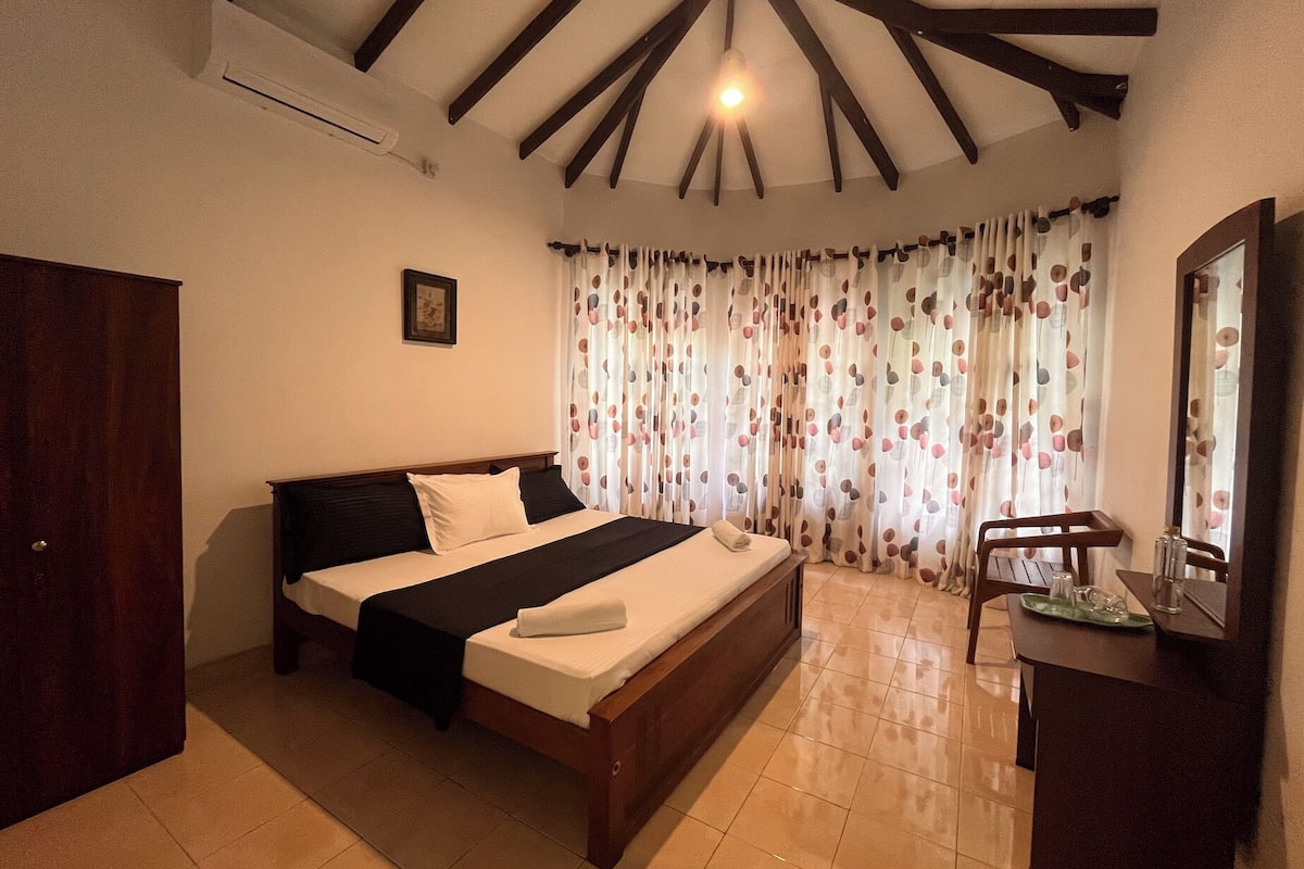 A bedroom with a bed, a wooden wardrobe, a desk with a mirror, and a window with curtains.