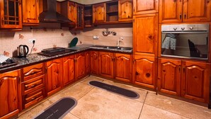 A kitchen with wooden cabinets, a stove, a sink, and a countertop. - Greenbell Kandy (Kandy)