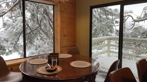 Ein Essbereich mit rundem Tisch, Stühlen und einer Chandelier. Große Fenster bieten Blick auf schneebedeckte Bäume.