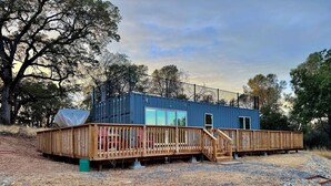 A modern blue building with a wooden deck and a staircase leading to a glass door. - Unique Container Home · 20 Acres · Starry Nights · EV Charger (Placerville)