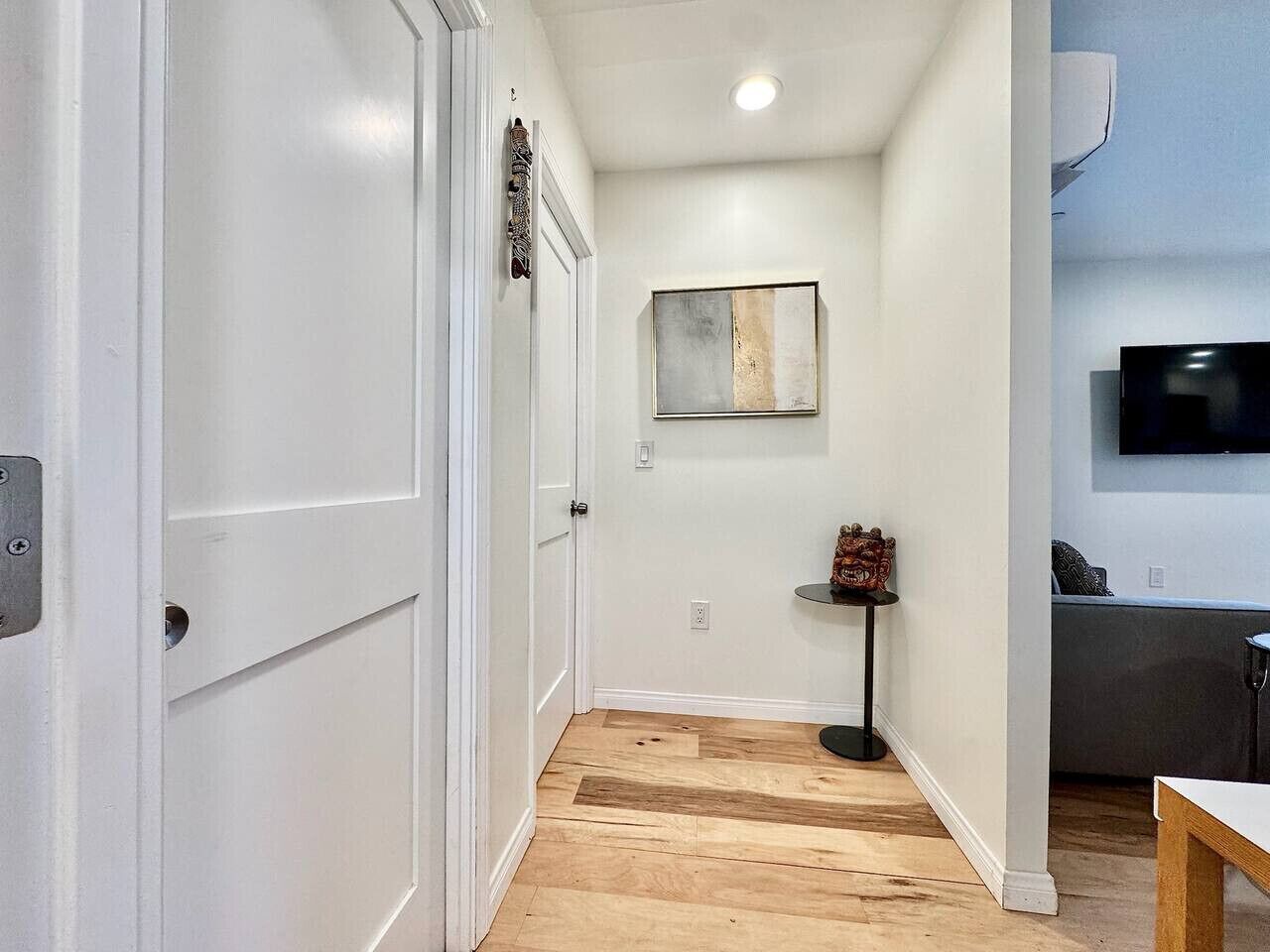 A hallway with white doors, a small table with a decorative item, and a flat-screen TV mounted on the wall.