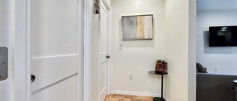 A hallway with white doors, a small table with a decorative item, and a flat-screen TV mounted on the wall.