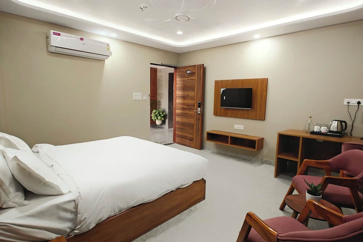A modern hotel room with a bed, wooden furniture, a TV, and a small kitchenette.