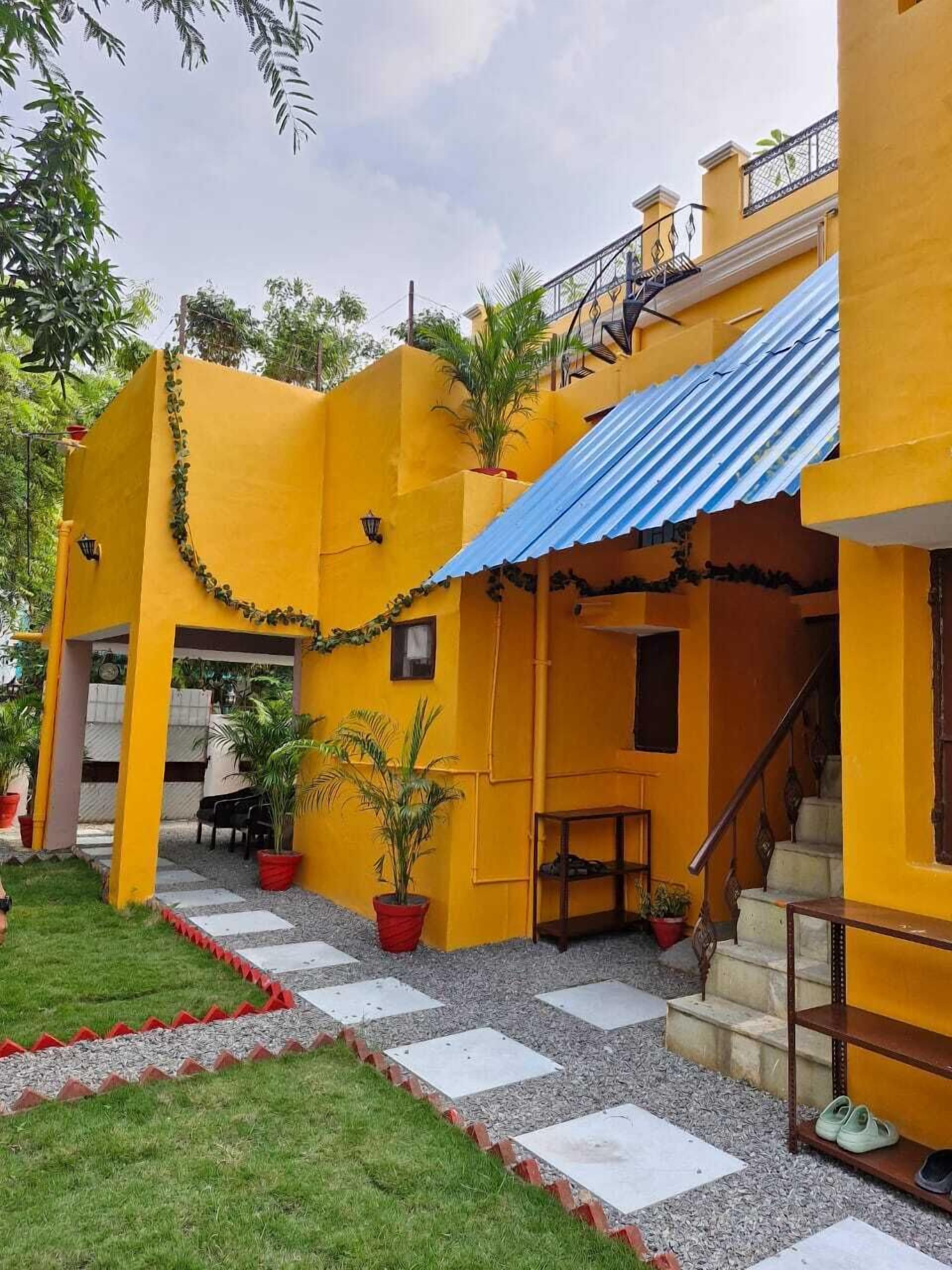 A yellow building with a blue roof, a staircase, and potted plants.