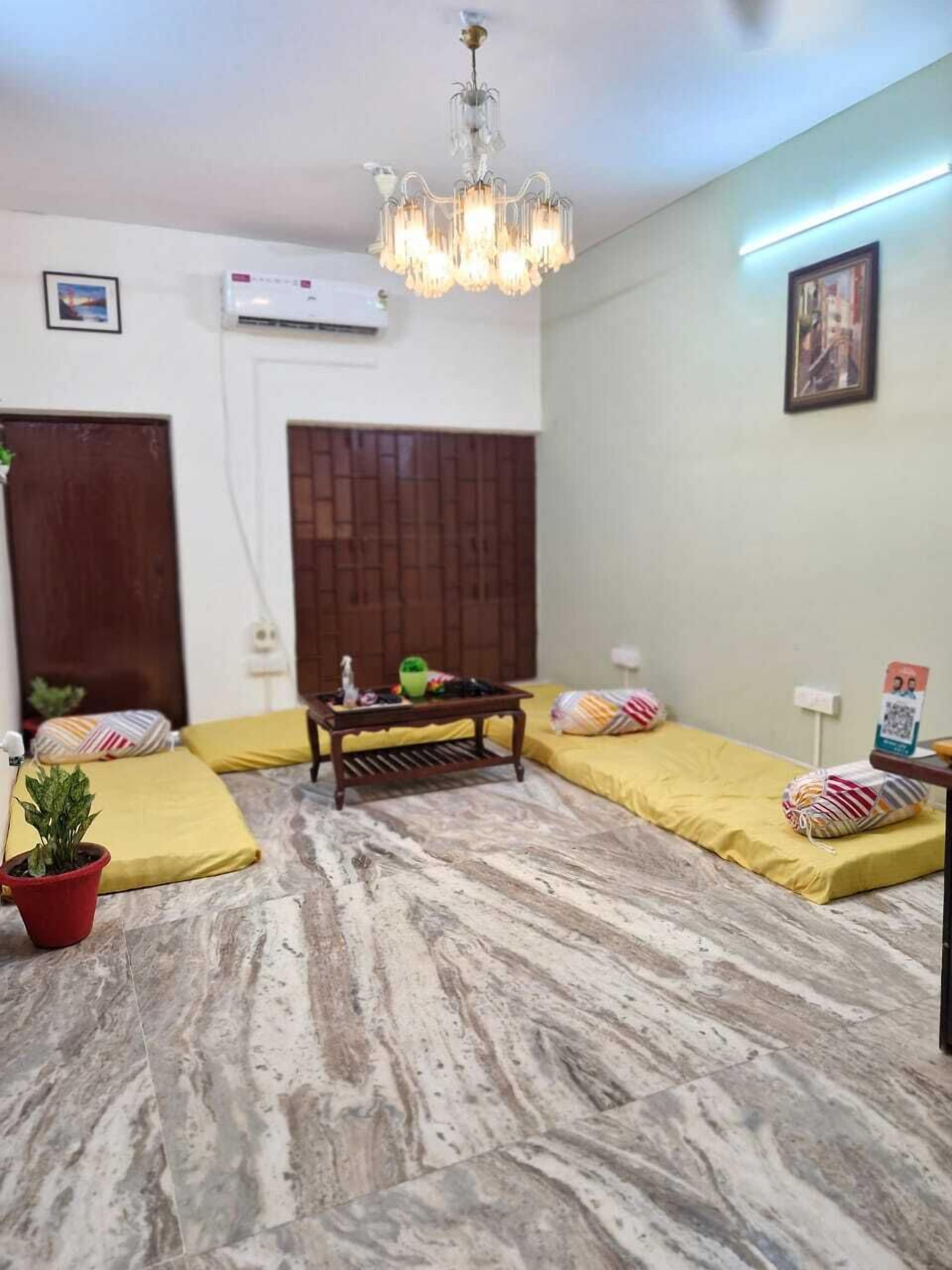 Una habitación con suelo de mármol, dos camas amarillas con almohadas, una mesa de centro de madera, un candelabro y un cuadro en la pared.