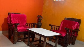 A room with two wooden chairs covered in red fabric, a small table, and a window with a decorative arch. - Coorg Heaven Home Stay (Madikeri)