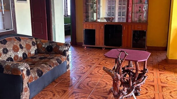 A living room with a patterned sofa, a wooden cabinet with glass doors, and a unique wooden coffee table. - Coorg Heaven Home Stay (Madikeri)