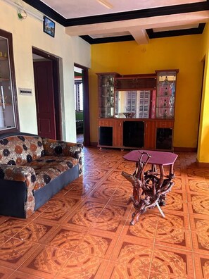 A living room with a patterned sofa, a wooden cabinet with glass doors, and a unique wooden coffee table. - Coorg Heaven Home Stay (Madikeri)