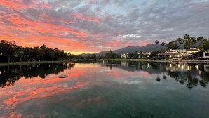 A serene lakeside view with a sunset, calm water reflecting the sky, and buildings in the background.