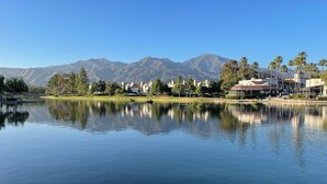 A calm lake with a reflection of buildings and mountains in the background.