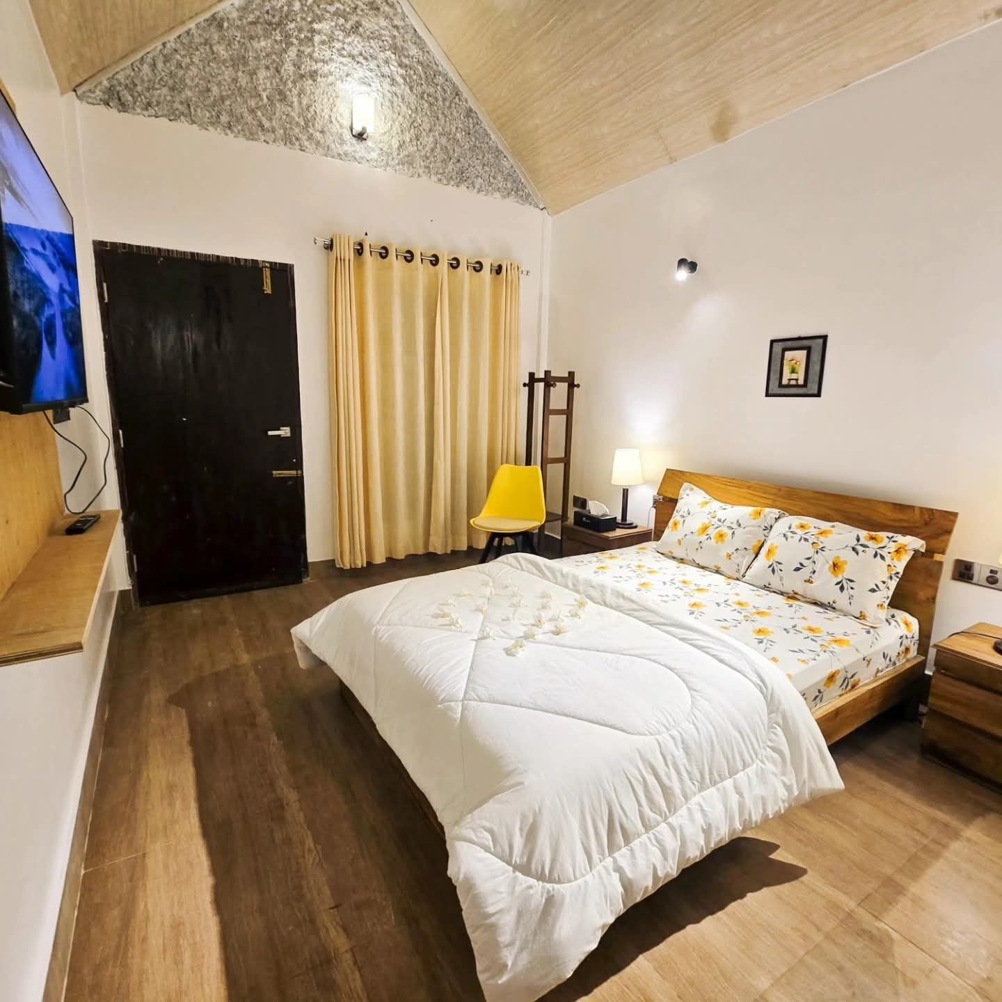 A bedroom with a bed, a desk, a chair, a TV, and a door.