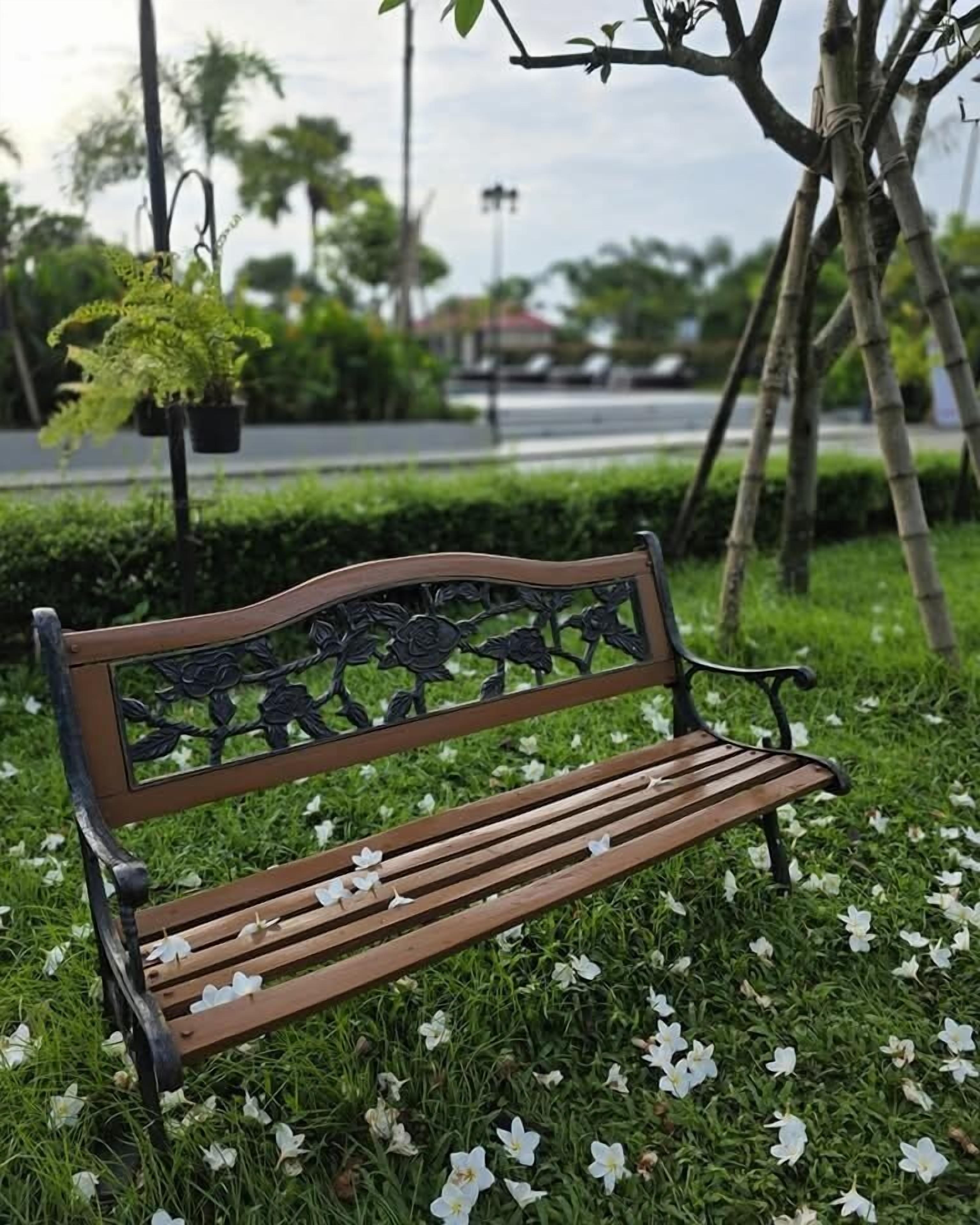 A wooden bench with metal backrest and armrests, surrounded by grass and white flowers.