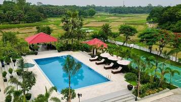 Piscina com espreguiçadeiras e guarda-sóis, cercada por vegetação e vista para o campo.