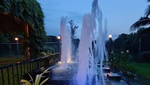 A nighttime outdoor water feature with multiple fountains, surrounded by greenery and a paved walkway. - Garden Centre Resort (Kaliganj)