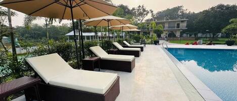 A poolside area with lounge chairs and umbrellas, a swimming pool, and a building in the background.