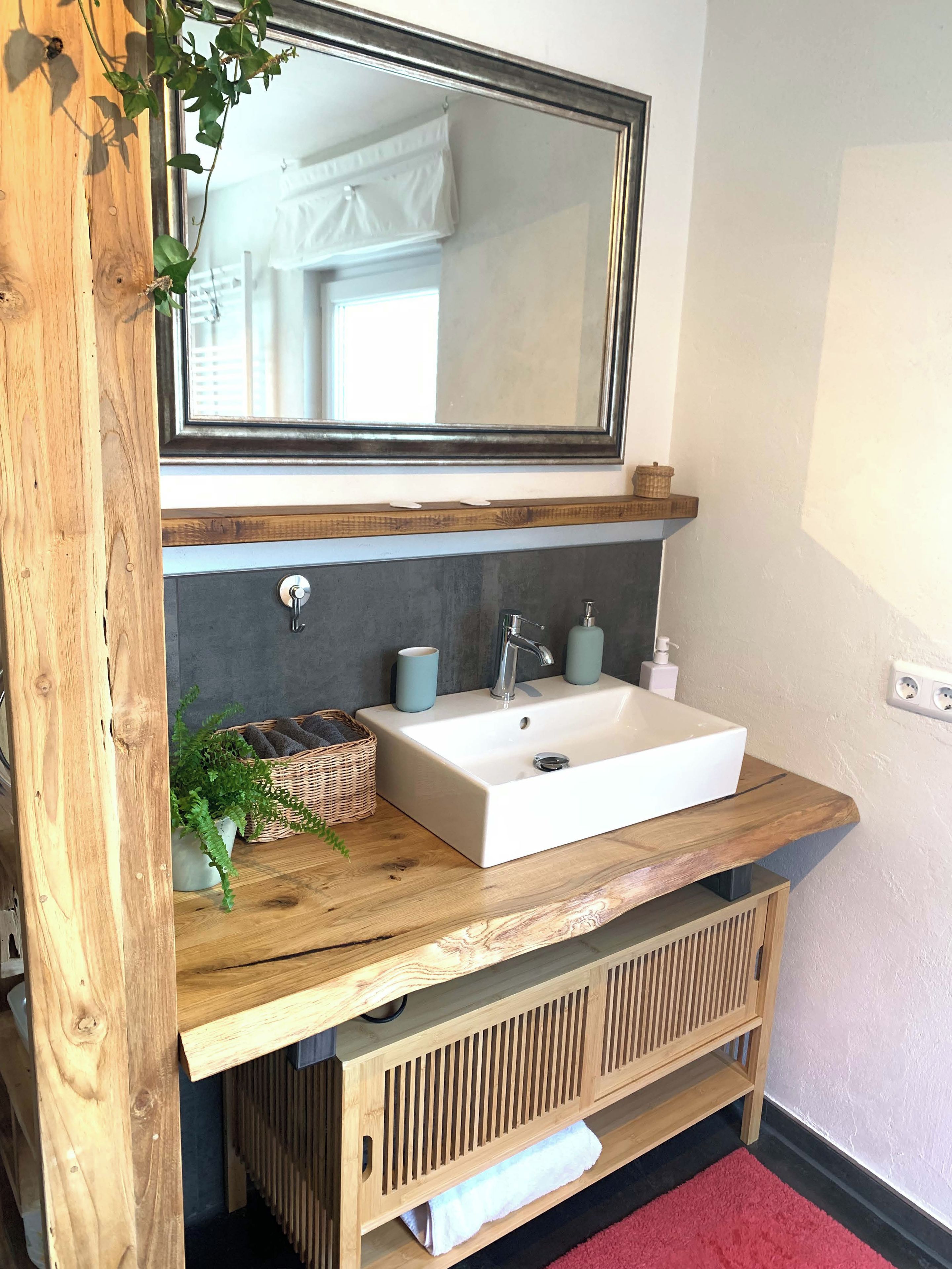 A bathroom with a wooden vanity, a white sink, a mirror, and a red rug.