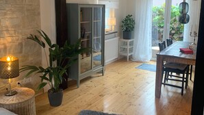 Ein geräumiger Wohnbereich mit Holzboden, einem blauen Teppich, einem Esstisch mit Stühlen, einer Glasschrank und einer Topfpflanze.