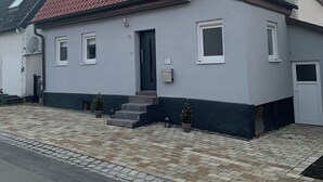 Ein eingeschossiges Haus mit rotem Ziegeldach, einer kleinen Veranda und einer sichtbaren Satellitenschüssel.