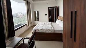 Une chambre d’hôtel comprenant un lit, un bureau, une chaise, une armoire, un ventilateur de plafond et une fenêtre avec des rideaux.