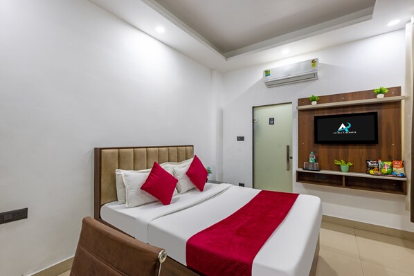 Une chambre d’hôtel moderne équipée d’un lit, d’un téléviseur fixé au mur et d’une petite étagère avec des en-cas.