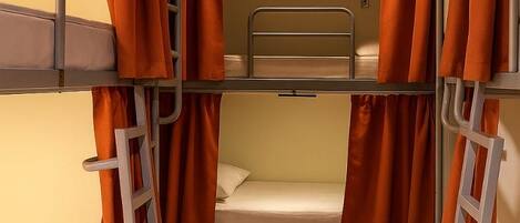 A bunk bed room with orange curtains, a ladder, and a light fixture on the ceiling.