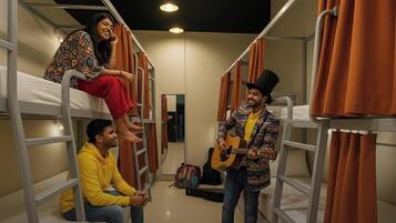 A dormitory room with bunk beds, a guitar player, and a person sitting on a bunk.