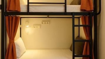 A bunk bed with orange curtains, a wall-mounted light, and a backpack on the floor.