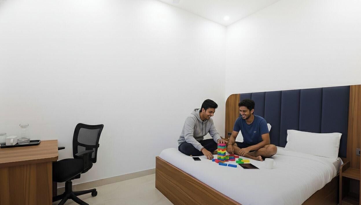 A bedroom with a bed, a desk, and two people playing with building blocks.