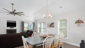 Un salon moderne avec une cheminée, un coin repas avec des chaises blanches et un ventilateur de plafond.