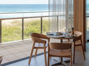 Un comedor con vistas al océano, que incluye una mesa redonda con sillas, un jarrón y una copa de vino.