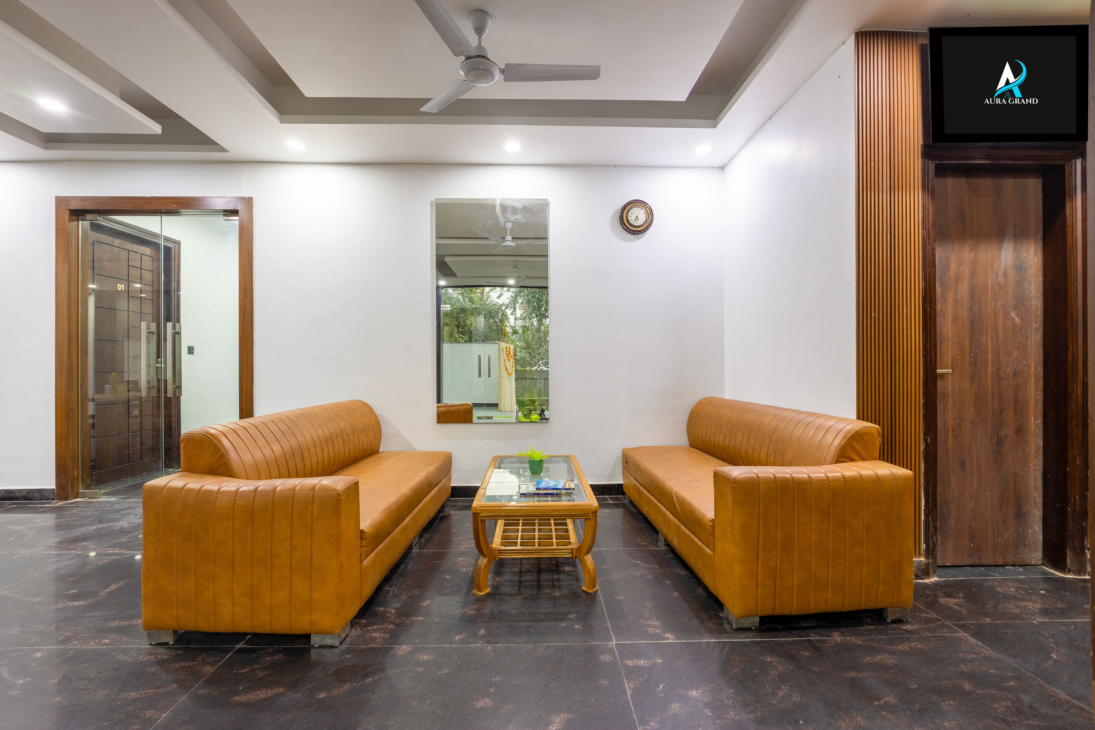 A lobby with two sofas, a coffee table, a ceiling fan, a clock, and a wooden door.