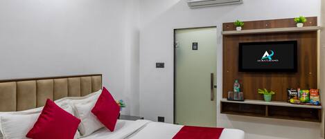A hotel room with a bed, a ceiling fan, a TV mounted on the wall, and a small shelf with snacks.