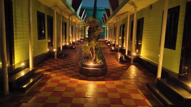A corridor with checkered flooring, a central planter with a tree, and a row of rooms on either side. - Shree Ram Swaroop vatika (Karwi)