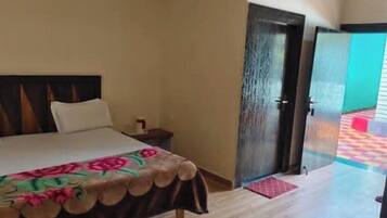 Una habitación de hotel con cama, mesita de noche y puerta que da a un pasillo con piso colorido.