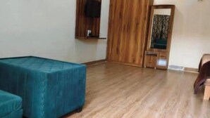A room with a wooden floor, two teal upholstered sofas, a wooden wardrobe, and a mirror. - Shree Ram Swaroop vatika (Karwi)