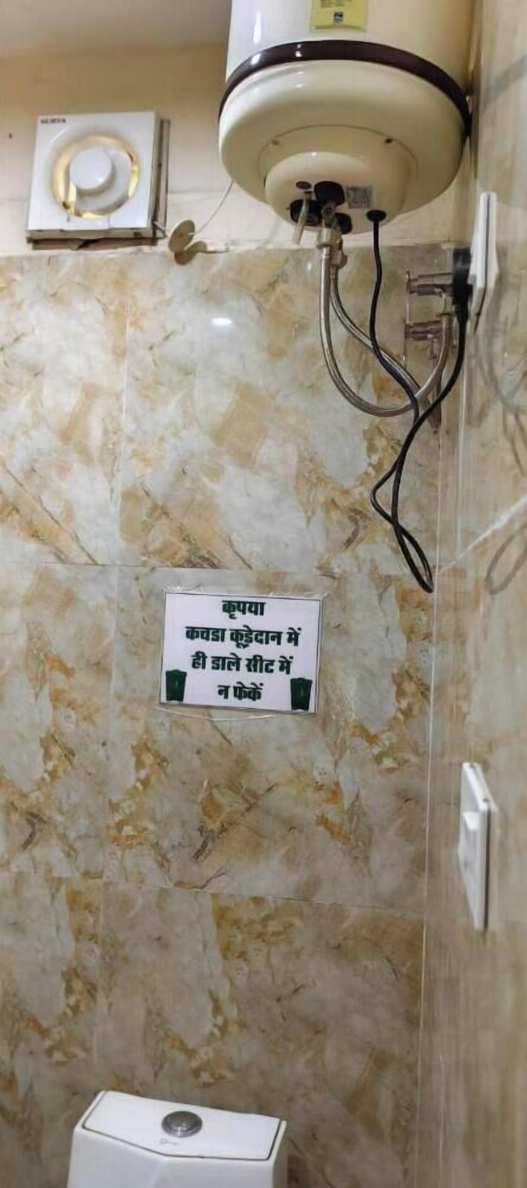 A bathroom with a marble wall, a hand dryer, a sign with text, and a toilet.