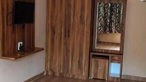 A room with a wooden floor, a ceiling fan, a mounted TV, and a built-in wooden cabinet. - Shree Ram Swaroop vatika (Karwi)