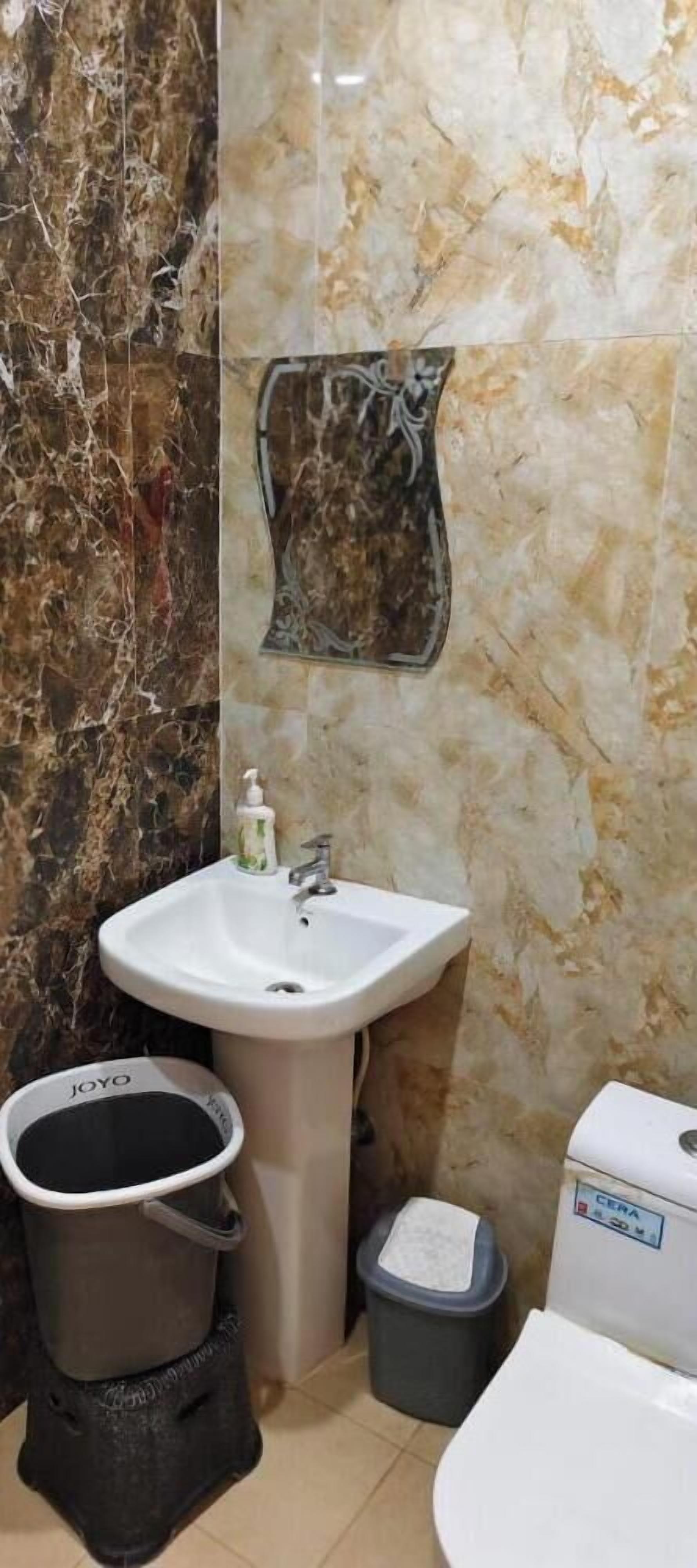 Un baño con un lavamanos blanco, un adorno en la pared, un cesto de basura y un inodoro.