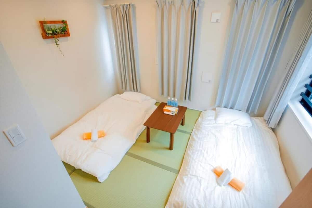 Una habitación de hotel pequeña con dos camas, una mesita y una ventana con cortinas.