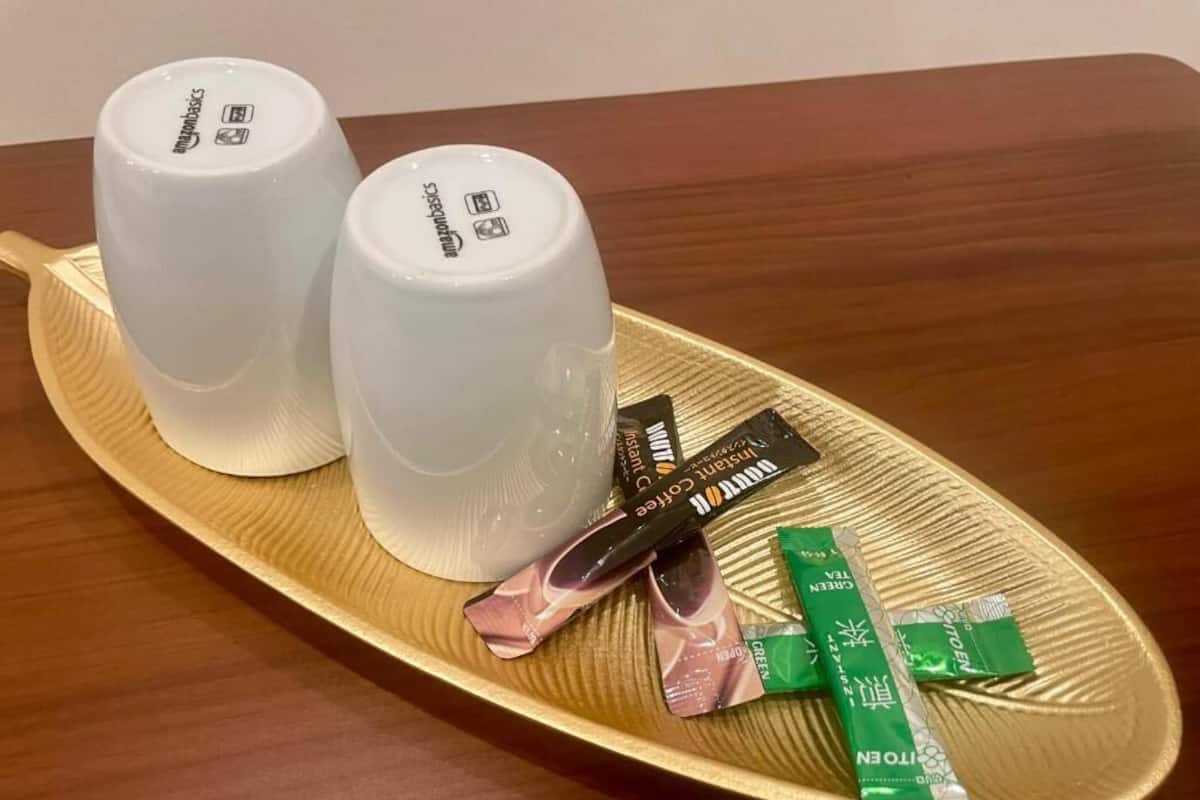 Dos tazas blancas sobre una bandeja dorada con algunos paquetes de comida.